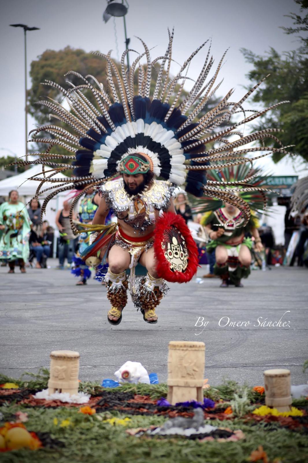 Aztec dancer leaping over ofrenda with white and red feathered headdress